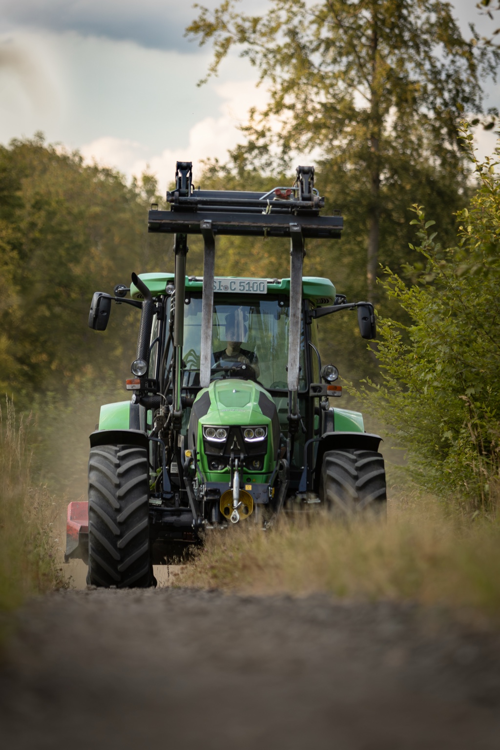 Grüner Traktor mit Frontlader auf einem Waldweg